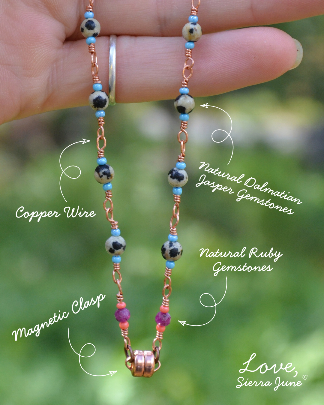 A close-up of a hand holding a beaded necklace with copper wire chains, dalmatian jasper gemstone beads, natural ruby gemstones, and a copper magnetic clasp, with handwritten text labels pointing to the materials.
