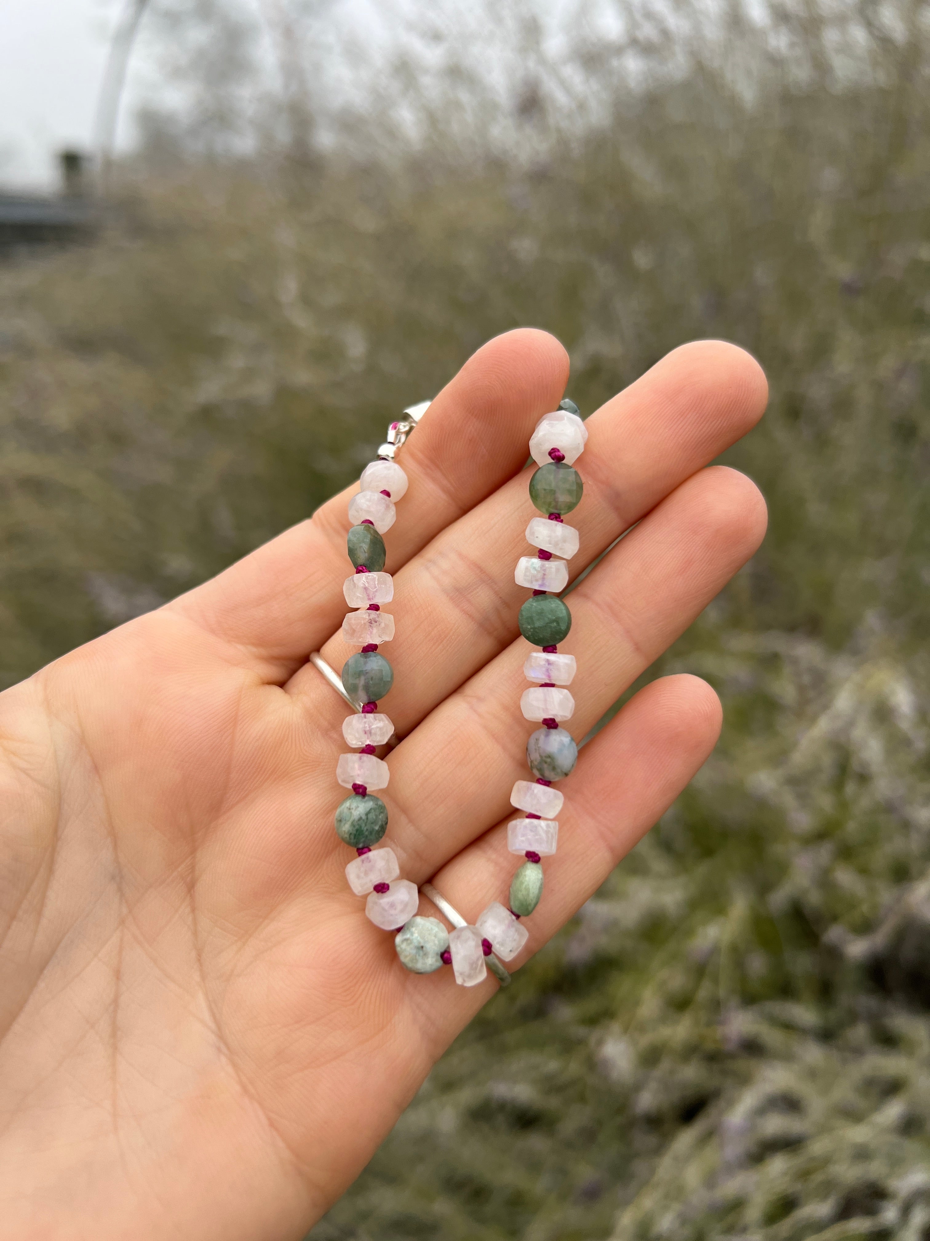 Hand holding a bracelet with small beads against a blurred natural background