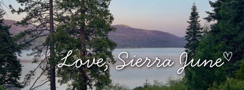 A scenic landscape photo of a calm lake surrounded by tall evergreen trees and distant mountains under a soft sky, with the white script text 'Love, Sierra June' overlaid across the center.